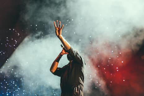 Photo d'un chanteur sur scéne levant les bras devant un écran de fumé