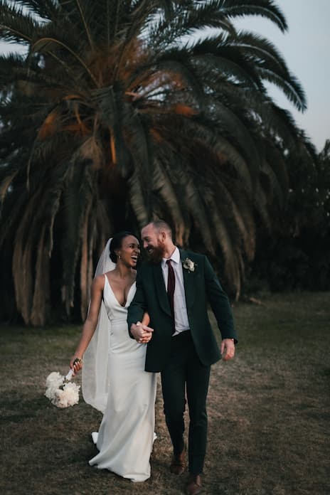 Photo d'un couple joyeux marchant devant des palmiers durant leur mariage
